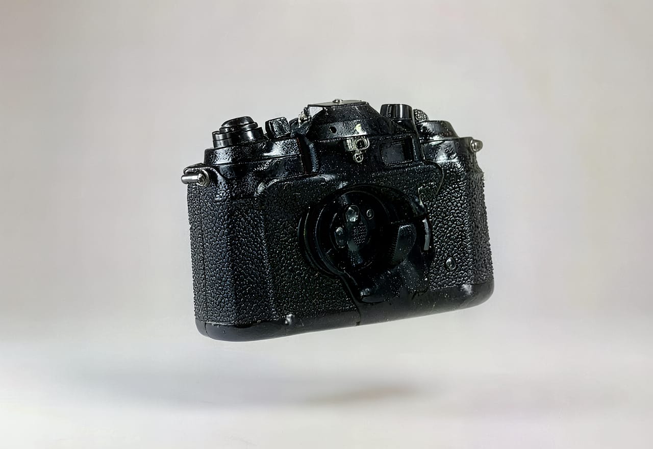 3D-render van een zwarte 35mm-spiegelreflexcamera met korrelige leerstructuur, zwevend boven een lichtgrijze achtergrond met zachte slagschaduw